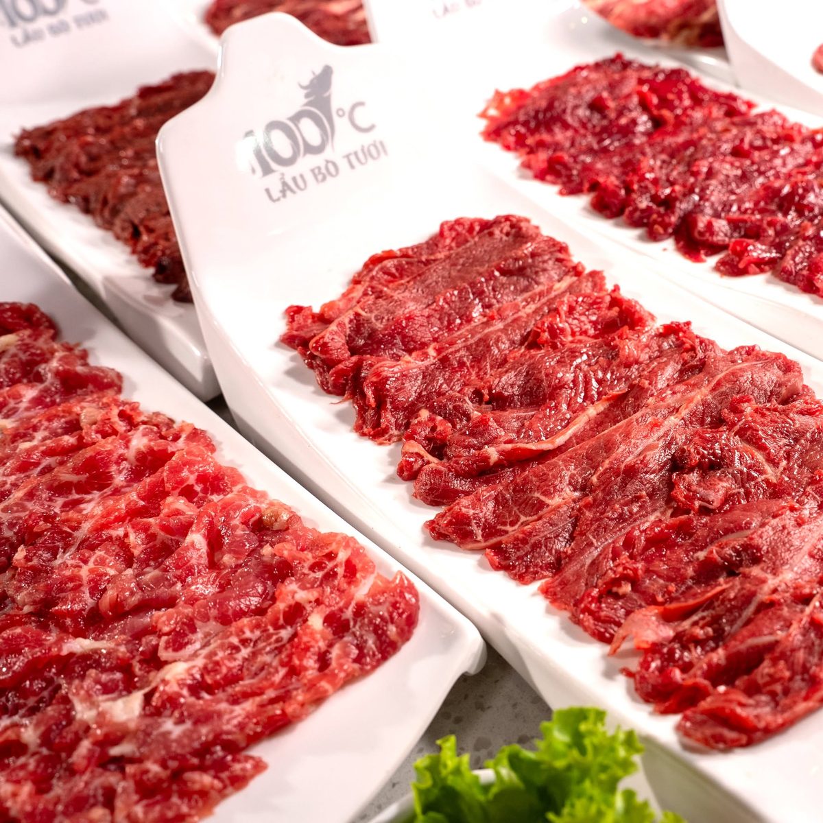 Đĩa thịt bò tươi thái lát trên đĩa sứ in logo 100°C